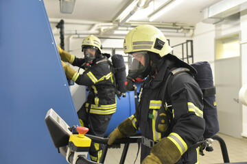 Two firefighters with respirator and air tank exercising in exercise room