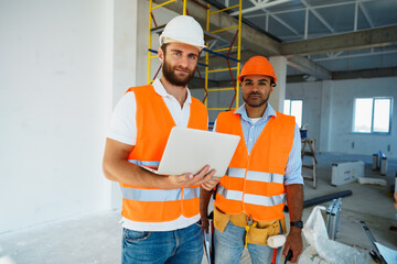 Two specialists supervisors in hardhats using laptop at construction site for work