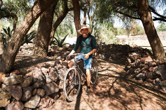 Mature man wearing hat riding bicycle on dirt road in Teotihuacan, Mexico