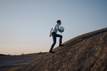 Mature businessman with laptop walking on a disused mine tip