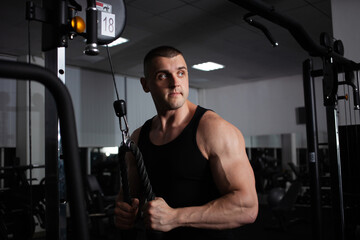Fototapeta na wymiar A sports athlete coach a muscular man does an exercise on a simulator in gym. Portrait, low key, darkness. builds up arm muscles