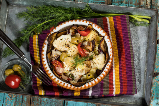 Casserole with aubergines, tomatoes, potatoes and green olives garnished with dill