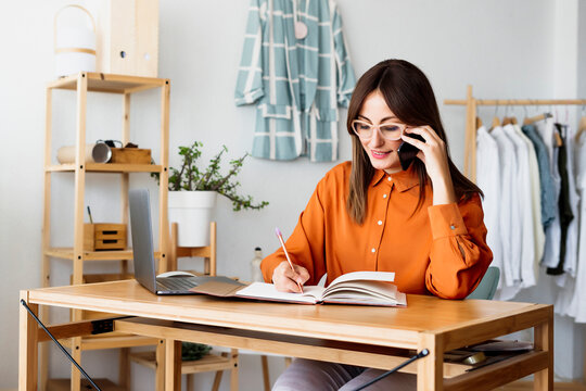 Female fashion designer working at home sitting at desk taking notes