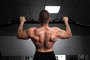 Fototapeta na wymiar A man athlete bodybuilder pulls up on his hands, builds muscles, does an exercise in gym. back