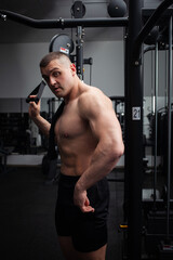 Fototapeta na wymiar Portrait of a beautiful male athlete bodybuilder in gym, low key, darkness. Posing, coach.