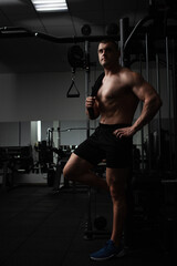 Fototapeta na wymiar Portrait of a beautiful male athlete bodybuilder in gym, low key, darkness. Posing, coach. standing