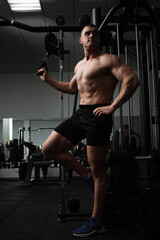 Fototapeta na wymiar Portrait of a beautiful male athlete bodybuilder in gym, low key, darkness. Posing, coach. press