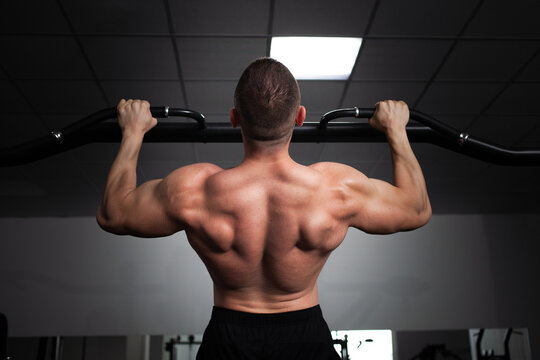 A man athlete bodybuilder pulls up on his hands, builds muscles, does an exercise in gym. back