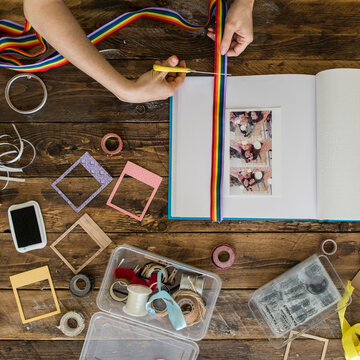 Top view of woman's hands decorating a photo album with a rainbow ribbon