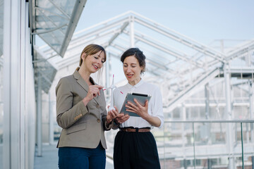 Two businesswomen with tablet and wind turbine model having a meeting at a greenhouse