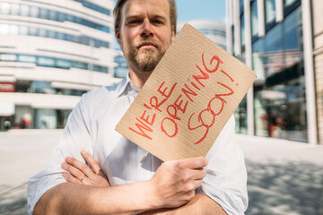 Shopkeeper holding cardboard with opening announcement in the city
