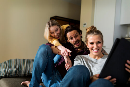 Friends sitting on couch in livingroom, having fun, using laptop