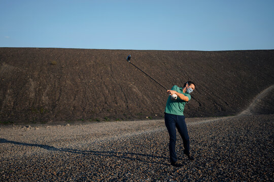 Mature man with a mask playing golf on a disused mine tip