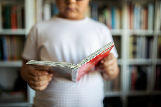 Boy standing in front of book shelves holding a book, close-up