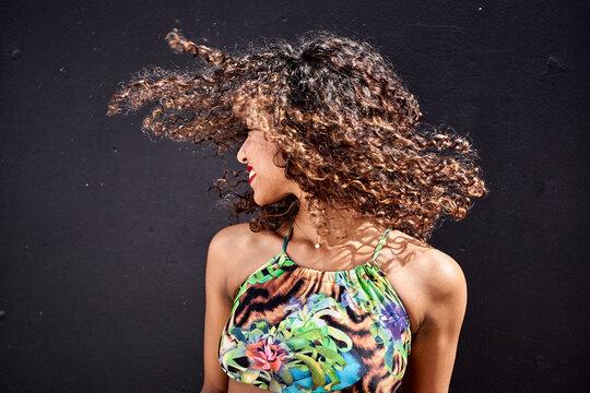 Smiling young woman tossing her curly hair in front of dark background