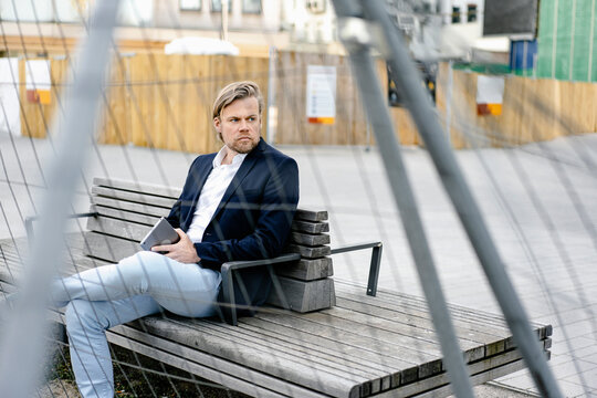 Businessman sitting on a bench behind ramshackle hoarding