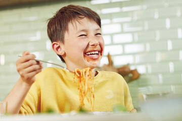 Messy boy eating spaghetti with tomato sauce