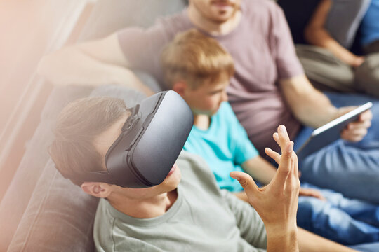 Happy family sitting on couch, using VR goggles and mobile devices