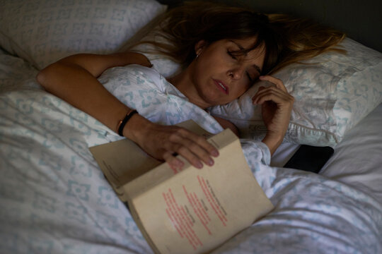 Woman asleep after reading a book in the bed