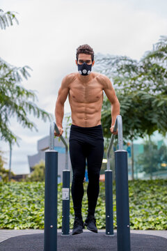 Athlete training on bars in the city, wearing breathing mask