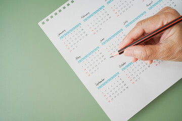 hand holding pencil with blurred yearly calendar for planning work ,monthly or yearly schedule , make appointment meeting ,manage timetable ,routine ,business project, timeline concept