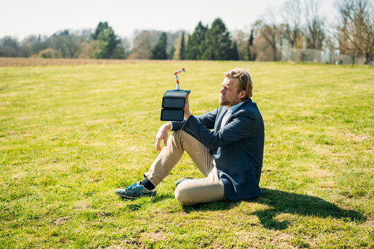 Businessman analyzing robot arm while charging with portable solar panel at park on sunny day