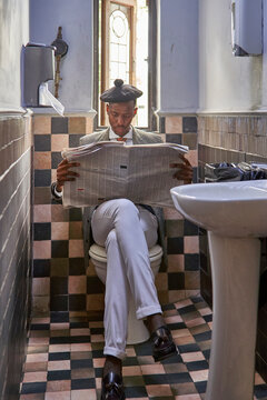 Stylish young businessman with a beret reading the newspaper sitting in the restroom