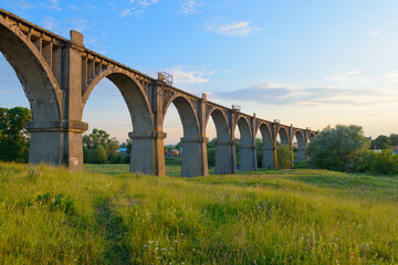 A long arched railway bridge over a green ravine on a summer evening