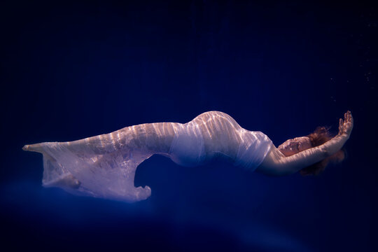 Pregnant woman wearing white dress under water