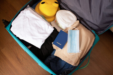 Top view of suitcase prepared for seaside holiday during a pandemic. Clothes, passport with medical and mask.