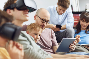 Happy family sitting on couch, using VR goggles and mobile devices