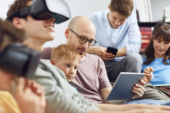Happy family sitting on couch, using VR goggles and mobile devices