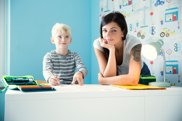 Portrait of mother with son doing homework at desk
