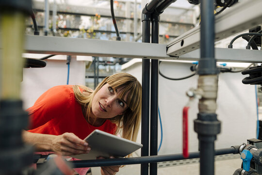 Female entrepreneur with digital tablet examining equipment in greenhouse