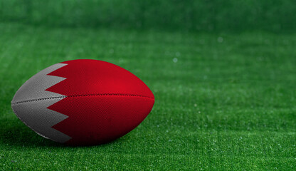 American football ball  with Bahrain flag on green grass background, close up