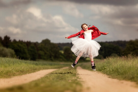 Portrait of happy girl wearing red leather jacket and tutu jumping in the air on dirt track