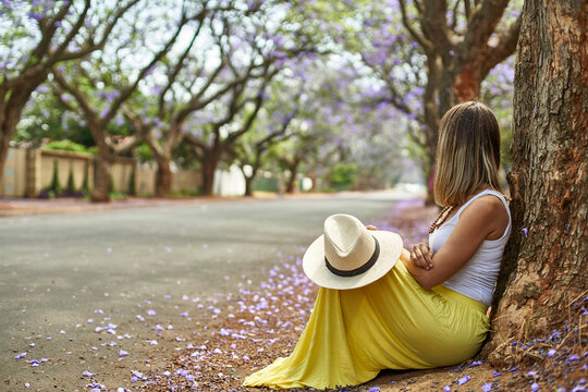 Woman leaning on a tree at a street with jacaranda trees in bloom, Pretoria, South Africa