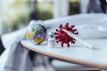 Model of coronavirus with vaccine on table with mini globe