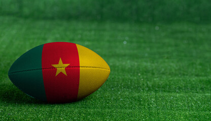 American football ball  with Cameroon flag on green grass background, close up