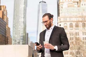 Bearded young businessman with coffee to go looking at cell phone, New York City, USA