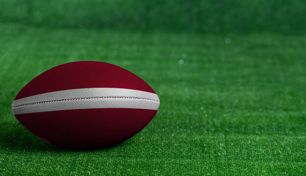 American football ball  with Latvia flag on green grass background, close up