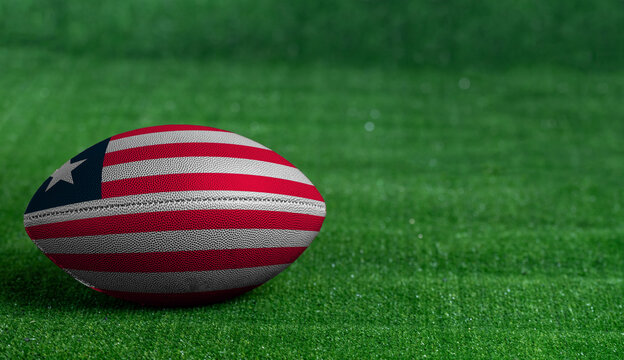 American football ball  with Liberia flag on green grass background, close up