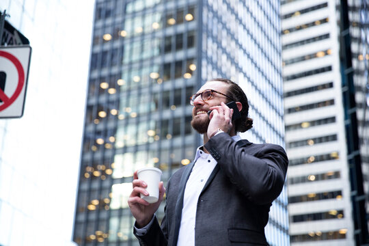 Happy young businessman with coffee to go on the phone, New York City, USA