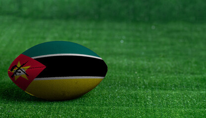 American football ball  with Mozambique flag on green grass background, close up