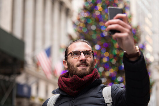 Portrait of tourist taking selfie with smartphone in front of lighted Christmas tree, New York City, USA