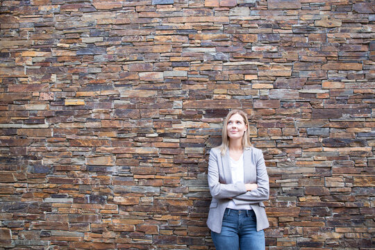 Woman in front of a wall looking upa, arms crossed