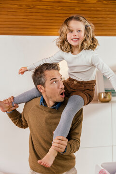 Happy father carrying daughter on shoulders at home