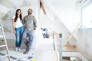 Portrait of confident couple standing in attic to be renovated