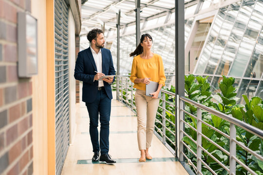 Male entrepreneur discussing while walking with female colleague in office corridor