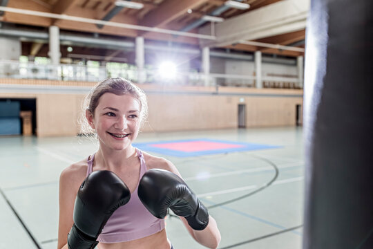 Smiling female boxer practising at punchbag in sports hall